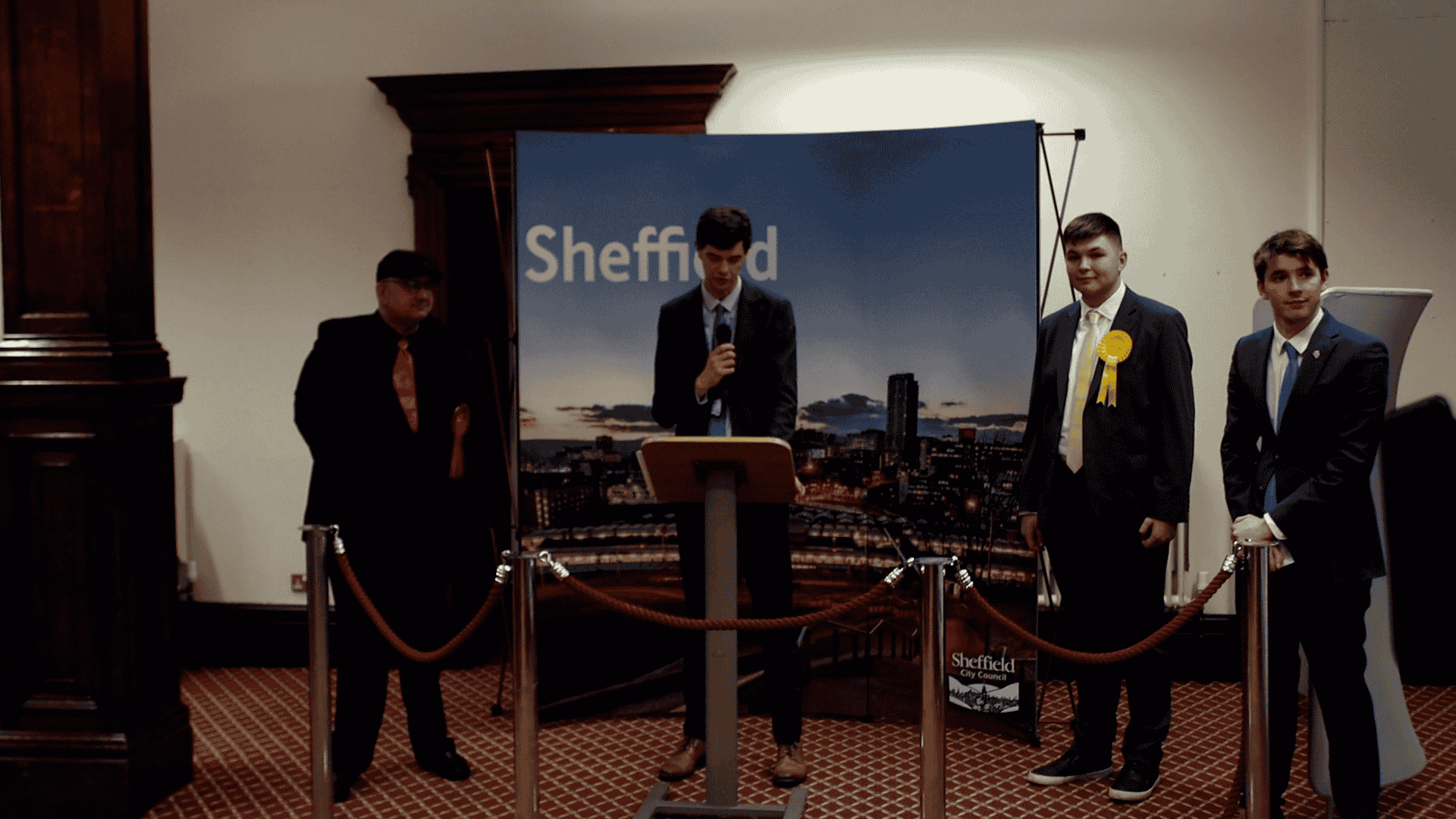 Three male candidates and a returning officer standing in front of a Sheffield City Council banner, as the by-election result is being announced