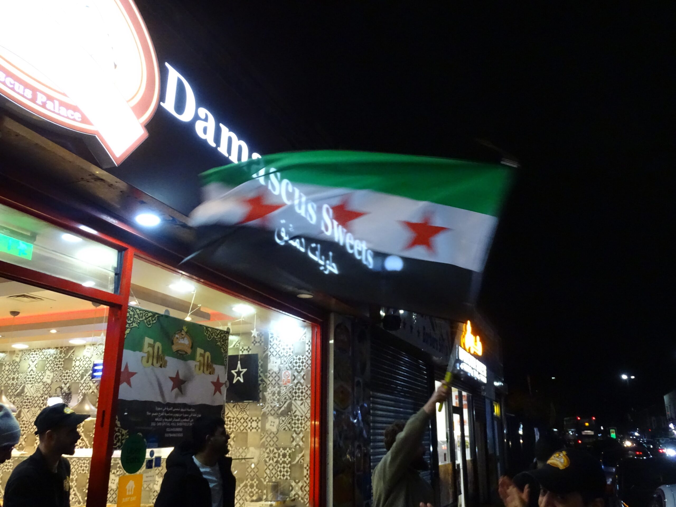 Syrians outside Damascus Bakery & Kitchen wave the Syrian revolutionary flag.