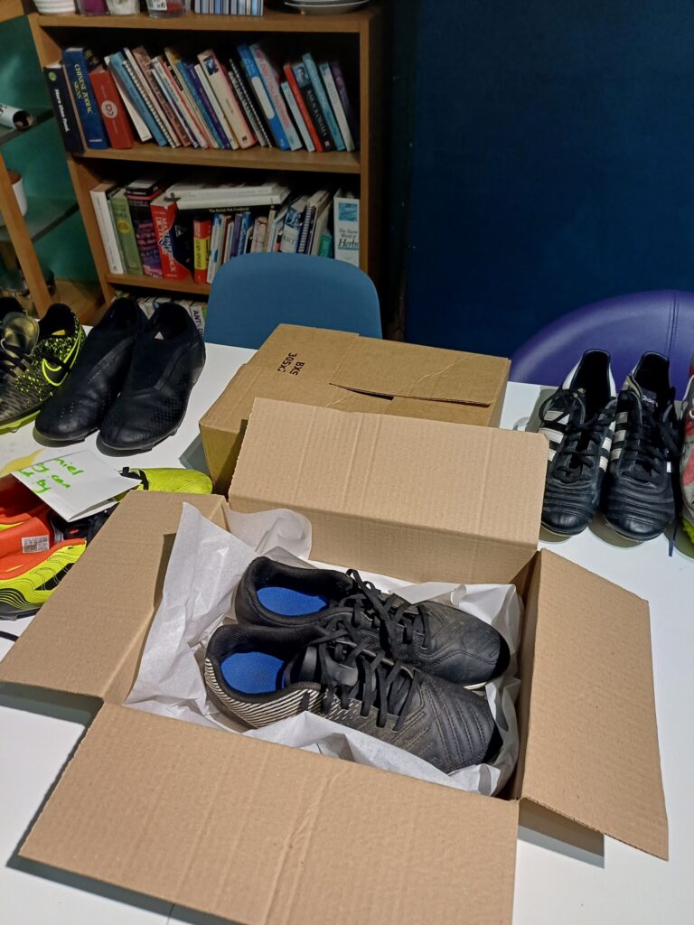 Pair of grey children's football boots in a cardboard box with tissue paper